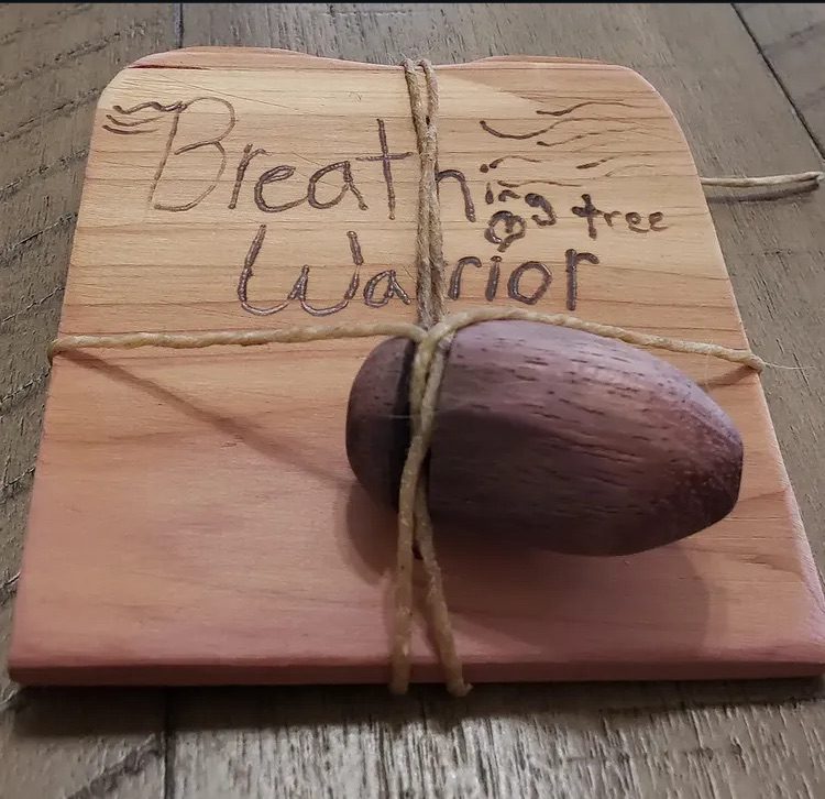 A walnut breathing tree tied with twine to a hand-burned cedar card reading Breathing Tree Warrior
